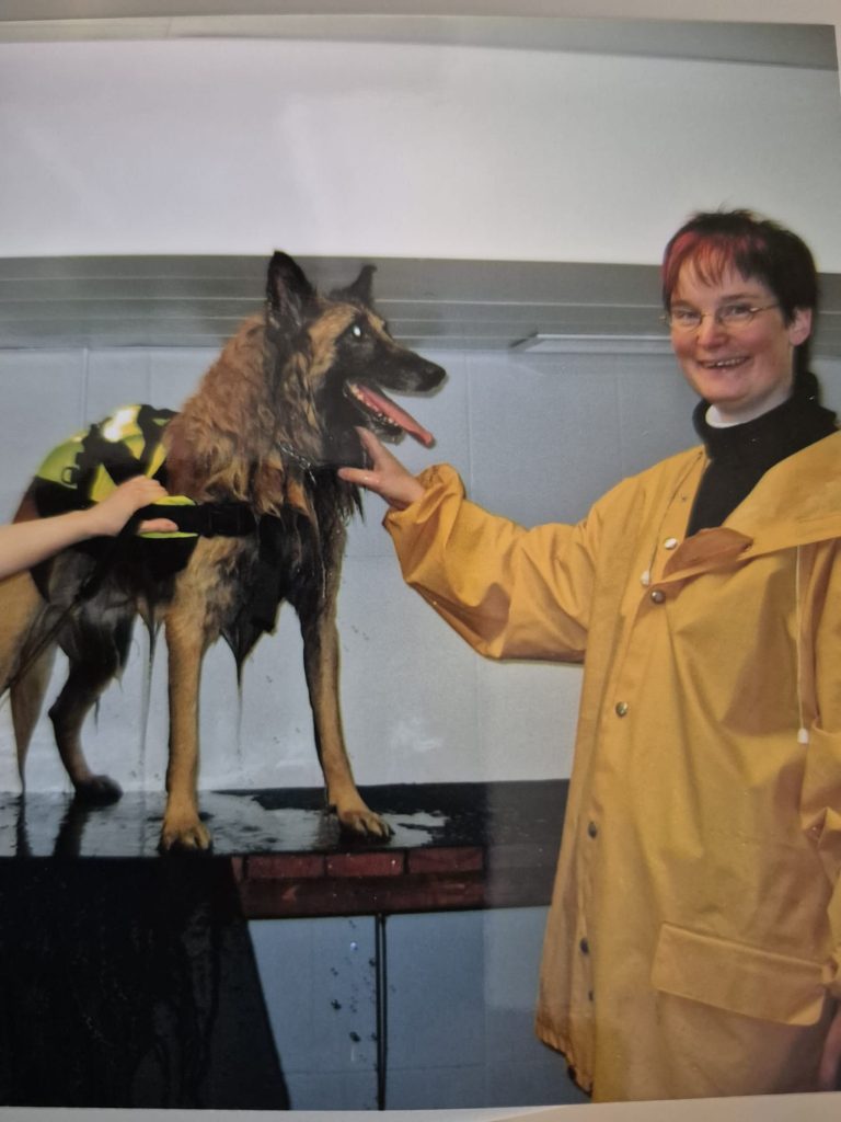 Nainen sadetakissaan koiran kanssa, joka käynyt uimassa